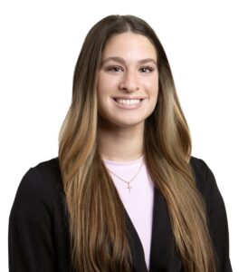 Portrait of Sydney Haubein smiling with long brown hair and black blazer.