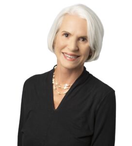 Portrait of a smiling mature woman with white hair in professional attire.