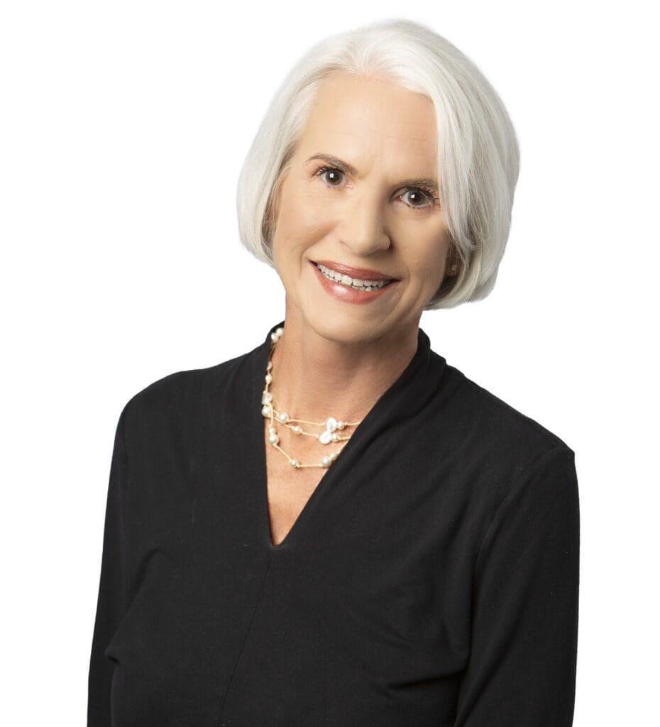 Portrait of a smiling mature woman with white hair in professional attire.